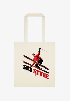 Persona che scia in discesa con giacca rossa e pantaloni neri, con la scritta "SKI STYLE" in nero e rosso su una borsa di tela beige.