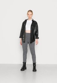 Camisa oversized em imitação de couro preto, top cropped branco, calças justas cinzentas aos quadrados e botas ankle pretas com fivela.