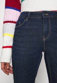 Mörkblå denimjeans med slim fit. Har kontrasterande gul söm, knäppning med knapp och en framficka.