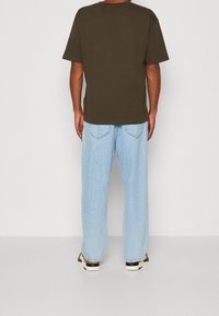 Olive green cotton T-shirt with a relaxed fit, paired with light blue wide-leg jeans. Casual shoes with a black and white color scheme.