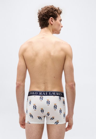 Νεαρός άνδρας εμφανίζεται από πίσω φορώντας λευκά boxer briefs Polo Ralph Lauren με σχέδιο ναυτικού μπλε αρκουδάκι και λογότυπο στη μέση.