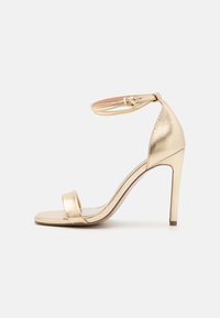 Guldmetalisk højhælet sandal med en tynd ankelrem, åben tå og slank stiletto-hæl. Glat overflade og minimale designdetaljer.