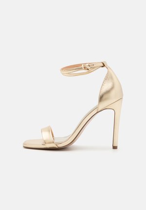 Goldfarbene, metallische High-Heel-Sandale mit einem dünnen Knöchelriemen, offener Zehenpartie und schlankem Stiletto-Absatz. Glatte Oberfläche und minimale Designdetails.