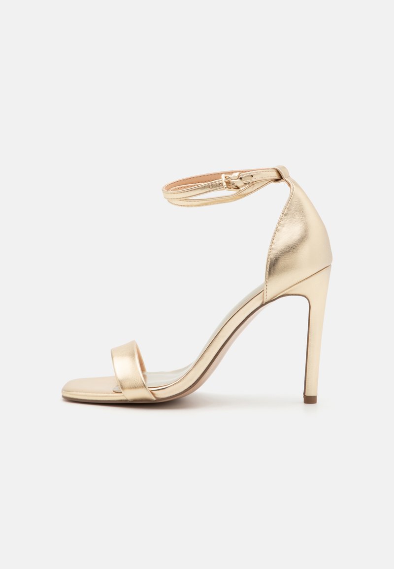 Guldmetalisk højhælet sandal med en tynd ankelrem, åben tå og slank stiletto-hæl. Glat overflade og minimale designdetaljer.
