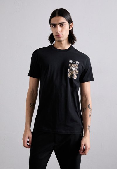 T-shirt en coton noir avec un graphique d'un ours sur la poitrine, avec le texte "Moschino" au-dessus de l'ours. Manches courtes et coupe classique.