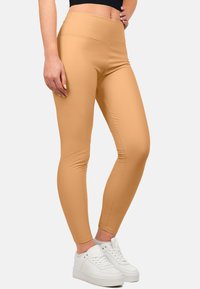 Leggings beige a vita alta con una texture liscia e un tessuto elastico, abbinati a sneakers bianche per un look informale.