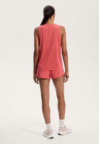 Ujjatlan rózsaszín sporttop perforált textúrával, hozzá illő shorts rövidnadrággal kombinálva. A modellt háttal állva fotózták.