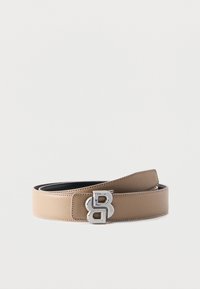 Ceinture en cuir beige enroulée avec une boucle argentée en forme de double lettre « B » sur fond blanc.