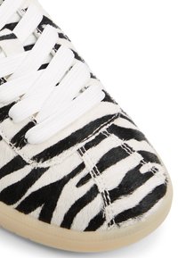 White sneaker featuring a black and white zebra stripe pattern, made of textured material with a rounded toe and flat rubber sole.
