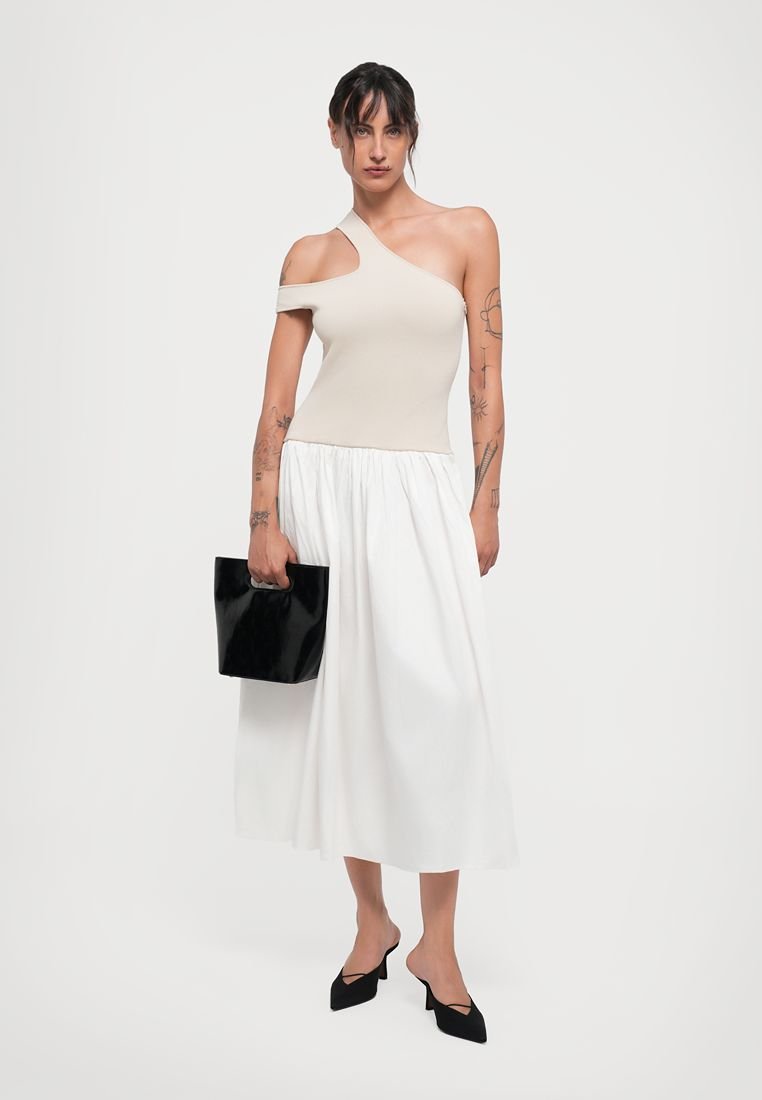 Haut beige à une épaule avec une coupe ajustée, associé à une jupe blanche fluide, un sac à main noir et des escarpins noirs à bout pointu.