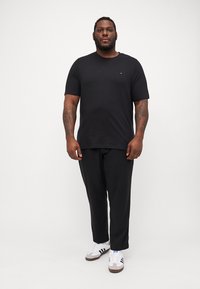 Svart t-skjorte med korte ermer og rund hals, sammen med løse svarte bukser og hvite joggesko med svarte og blå detaljer.