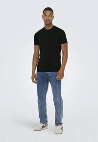 Sort kortærmet t-shirt lavet af blød bomuld, parret med lyseblå jeans og hvide sneakers med blå accenter. Simpelt design, slim fit.