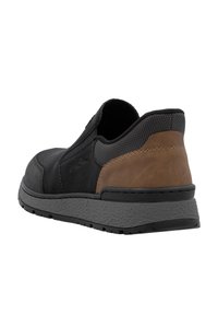 Zapato negro tipo slip-on con un upper de tela texturizada, acento de cuero marrón en el talón y una suela gris texturizada y acolchada.