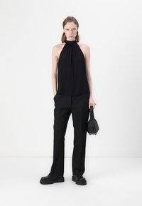 Mustatolkku hihaton paita, jossa on ryppyinen pääntie, yhdistettynä löysiin mustiin housuihin ja pieneen mustaan käsilaukkuun. Silkkinen texture, minimalistinen muotoilu.