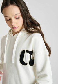 Witte hoodie van zacht materiaal met een groot, geborduurd zwart logo op de borst. Voorzien van een trekkoord en een ontspannen pasvorm.