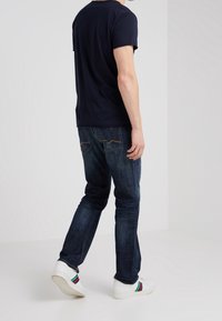 Námořnické tričko s krátkým rukávem spárované s tmavě modrými džíny. Bílé tenisky s barevnými pruhy. Jednoduchý, pohodlný a přiléhavý design.