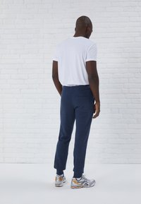 Jogging pants bleu marine avec une texture douce, une taille élastique et une poche latérale ; associés à un t-shirt blanc uni et des chaussures de sport.