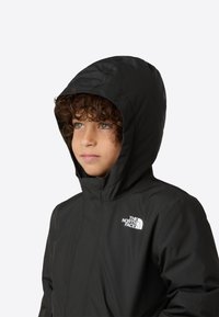 Veste noire imperméable avec capuche, texture lisse, arborant un logo blanc sur la poitrine gauche, et une fermeture éclair à l'avant.