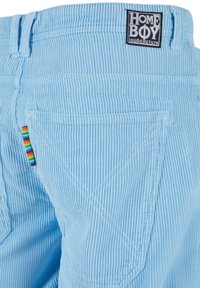 Light blue corduroy pants with a textured surface, featuring rainbow-striped stitching on the side and a prominent black logo label.