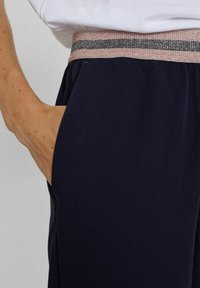 Kariniai kelnes su glotnia tekstūra, su rožiniu ir sidabriniu tekstūruotu elastiniu juosmeniu ir šoninėmis kišenėmis.