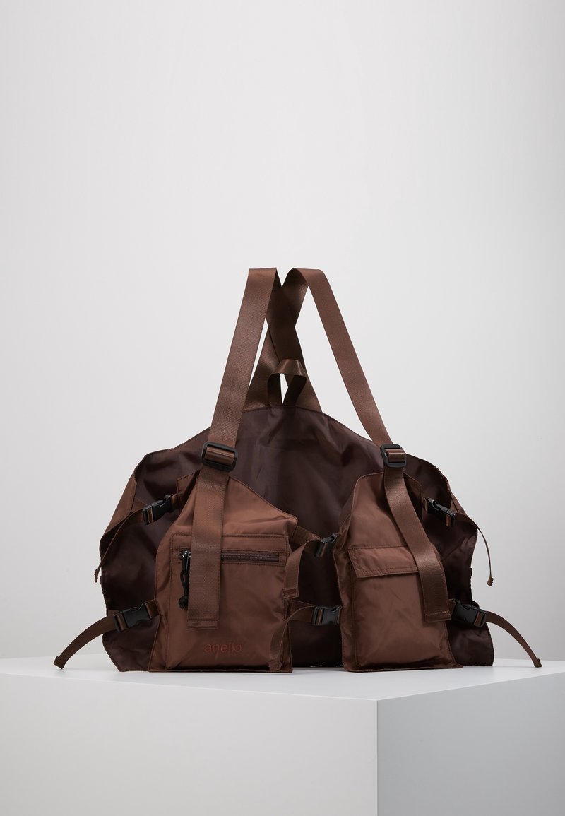 Brun nylon gympapåse med justerbara remmar, två sidofickor och dragkedjedetaljer. Mjuk textur och minimalistisk design.