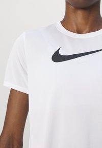 Balta Nike T-kreklu ar melnu swoosh logo, īsām piedurknēm, apaļu kakla izgriezumu un gludu, vieglu auduma tekstūru.