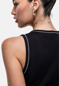 Czarny ribbed top na ramiączkach z kontrastującym białym przeszyciem, z okrągłym dekoltem i bezrękawowym fasonem, przedstawiony z boku.