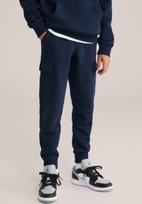 Marine cargo sweatpants met twee zijzakken, geribbelde boorden en een trekkoord in de taille, gecombineerd met zwart-witte sneakers.