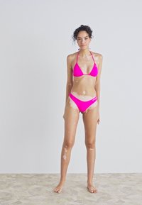 Svetlo roza bikini s trokutastim vrhom in hipster dnom. Gladka tekstura, minimalistična zasnova in prilagodljive naramnice.