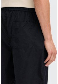 Black fabric pants with an elastic waistband and a single patch pocket on the back. The material has a soft texture and a relaxed fit.