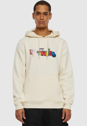 Cream-colored hoodie made of soft fabric, featuring a front pocket, drawstring hood, and colorful graphic "siTunis" on the chest.