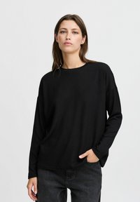 Maglietta nera a maniche lunghe con una vestibilità rilassata, realizzata in un tessuto a costine testurizzato e con scollatura rotonda. Abbinata a jeans scuri.