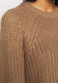 Brauner Strickpullover mit geripptem Rundhalskragen, strukturiertem Muster und lockerer Passform, der ein weiches und kuscheliges Erscheinungsbild zeigt.