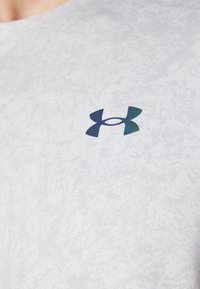 Camiseta atlética gris con un patrón texturizado, que presenta un logo azul y verde en el pecho. Mangas cortas y escote redondo.