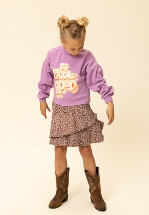 Paarse sweatshirt met de tekst "It Feels Good", gelaagde bloemenrok en bruine cowboylaarzen. Voorzien van een geplooide zoom en zachte stof.