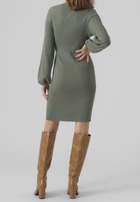 Robe longue à manches longues en tricot côtelé vert olive avec une silhouette ajustée. Associée à de hautes bottes en cuir marron clair avec un talon épais.