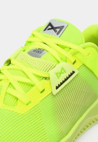 Νεον κιτρινό αθλητικό παπούτσι με διχτυωτό πάνω μέρος, υφαντές επενδύσεις και διακριτική σκούρα λογότυπη έμφαση στη γλώσσα. Οι κορδόνια ενσωματωμένα στο σχέδιο.