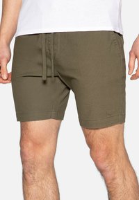 Grüne Shorts aus leichtem Stoff, mit einem elastischen Bund und Kordelzug, sowie einem kleinen Logo auf der Vorderseite.