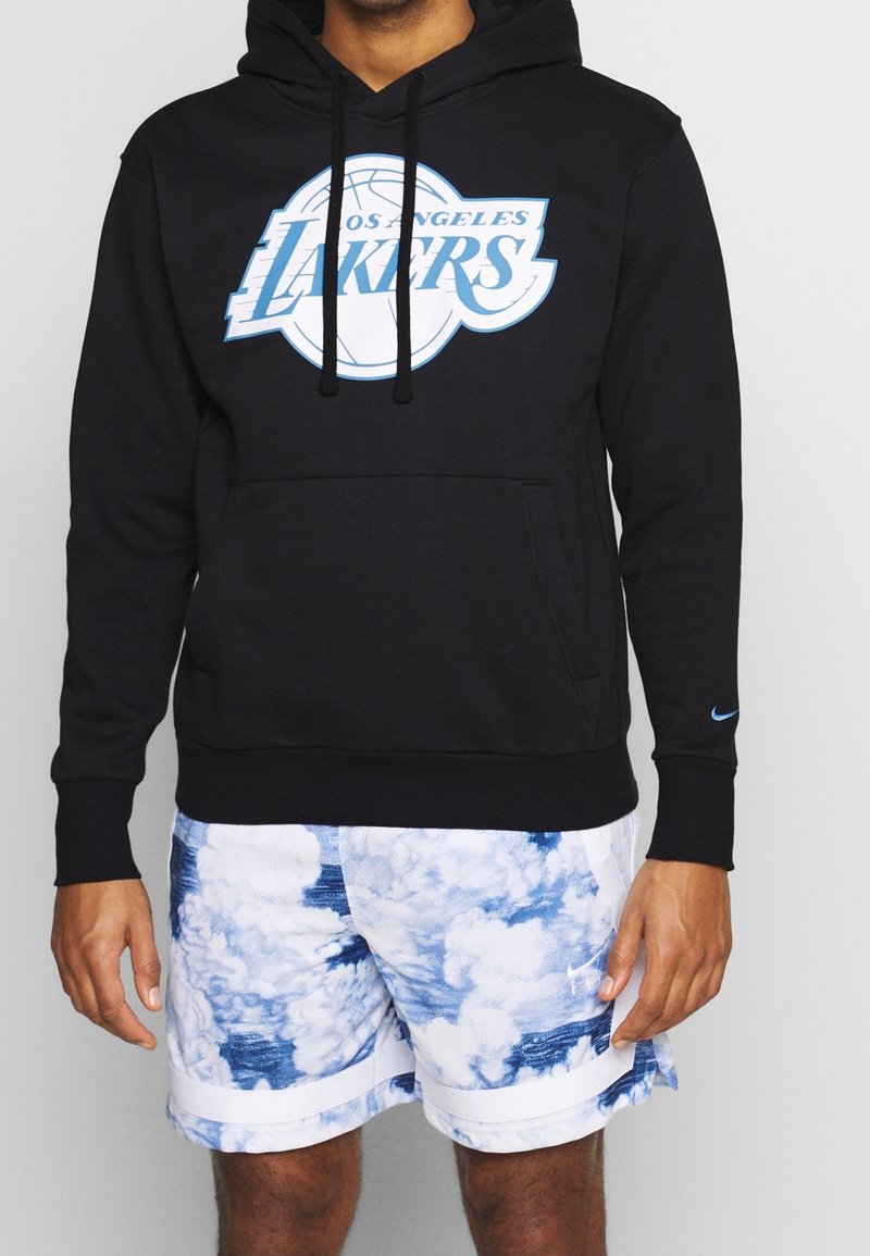 Czarna bluza z kapturem z logo Los Angeles Lakers w jasnoniebieskim kolorze, z kieszenią na froncie i sznurkiem do regulacji. W zestawieniu z białymi szortami w wzór chmur.