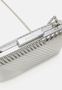 Srebrna metalowa torebka kopertówka z żebrowaną teksturą i łańcuszkiem. Posiada zapięcie na klamrę z wygrawerowanym napisem "ANNA FIELD" na elemencie metalowym.