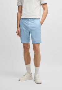 Ljusblå shorts i bomullsblandning med sidofickor, knappstängning och fållad avslutning. Bärs med vita sneakers och strumpor.