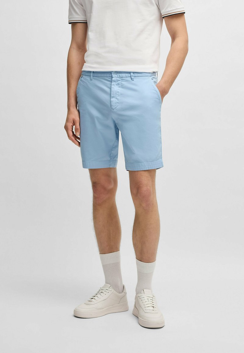 Ljusblå shorts i bomullsblandning med sidofickor, knappstängning och fållad avslutning. Bärs med vita sneakers och strumpor.