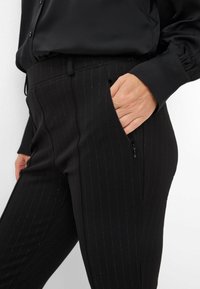 Zwarte pinstripe broeken van gestructureerde stof, voorzien van een zijrits- en een aansluitende pasvorm. Op maat gemaakt voor een strakke uitstraling.
