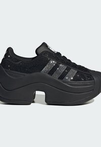 Black platform sneakers featuring a textured mesh upper with rhinestone accents and three black stripes on the side. Thick rubber sole.