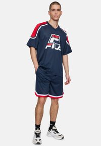 Morska siateczkowa uniform sportowy z wyraźnym logo, czerwonymi akcentami i białymi wykończeniami. Zawiera luźną koszulkę i pasujące szorty.
