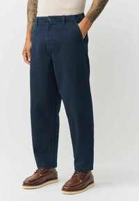 Navy blue cotton pants with straight-leg design, front pockets, and a button closure. Paired with brown leather lace-up boots.