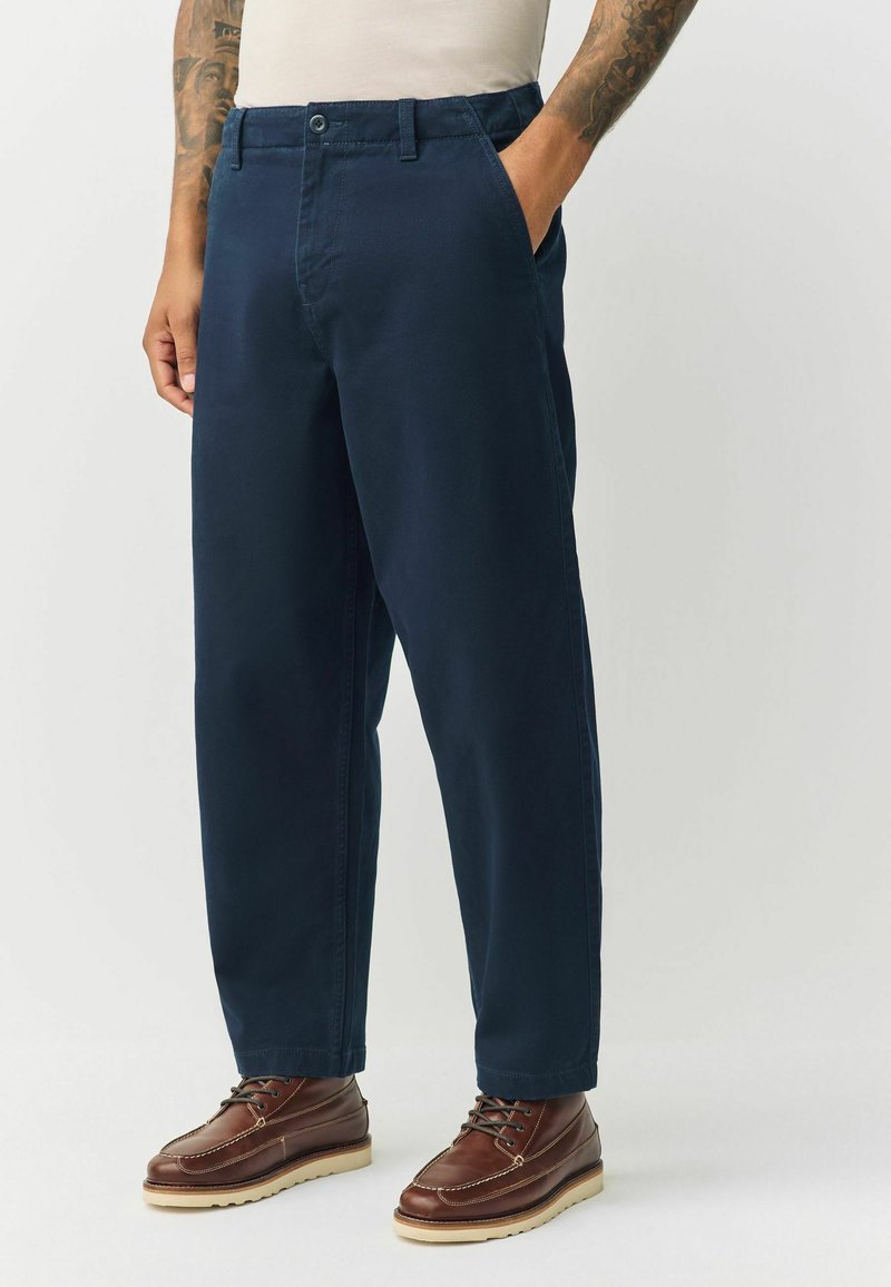 Navy blue cotton pants with straight-leg design, front pockets, and a button closure. Paired with brown leather lace-up boots.