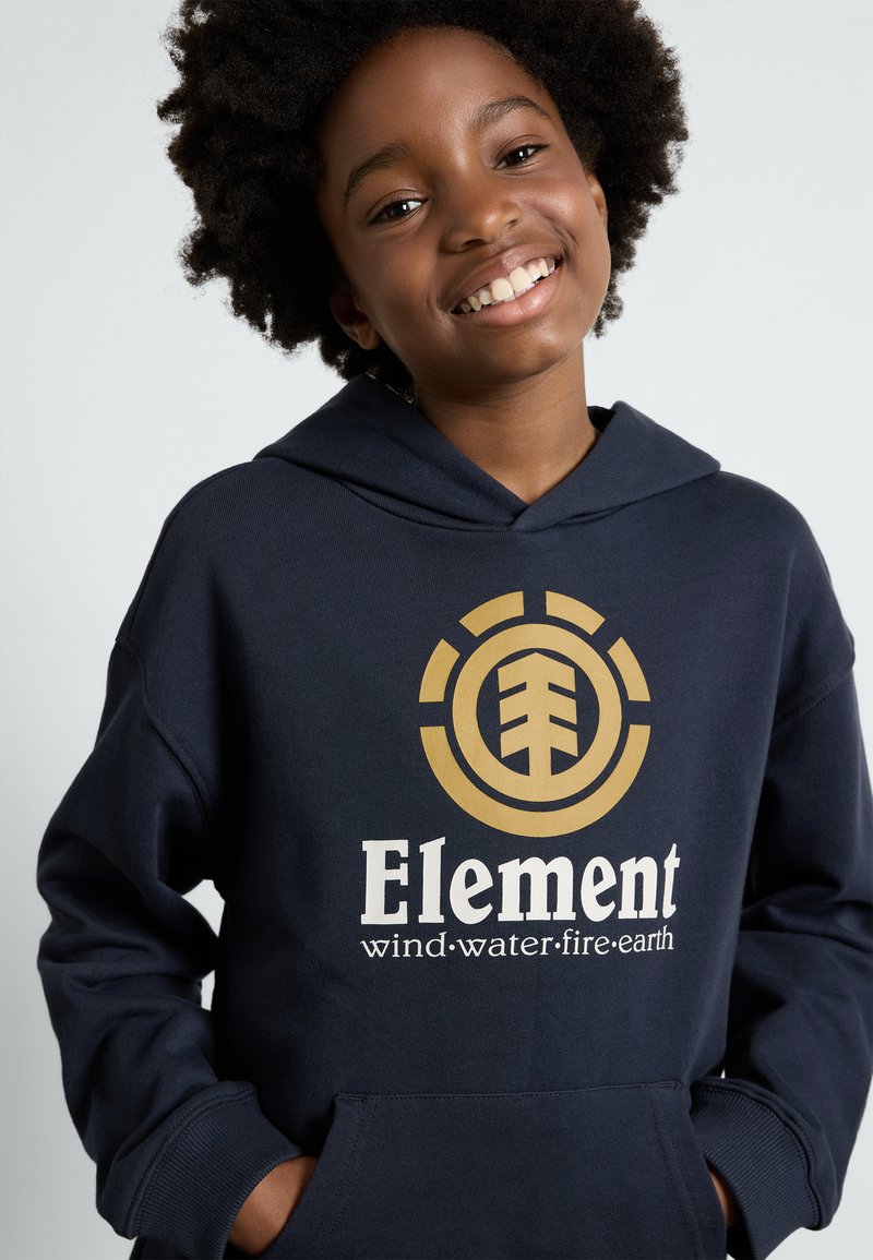 Felpa blu navy con logo di un albero dorato; testo bianco "Elementi vento.acqua.fuoco.terra." Design con cappuccio e tessuto testurizzato.