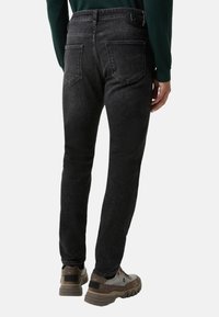 Černé džínové kalhoty s úzkým střihem, designem s pěti kapsami a černým knoflíkem v pase, doplněné o šedé a hnědé boty.