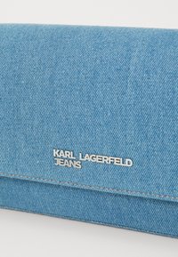 Denim torba za ključeve svijetloplave boje s dugmetom "KARL LAGERFELD JEANS" u srebrnoj boji. Ima čiste linije i teksturu karakterističnu za denim tkaninu.